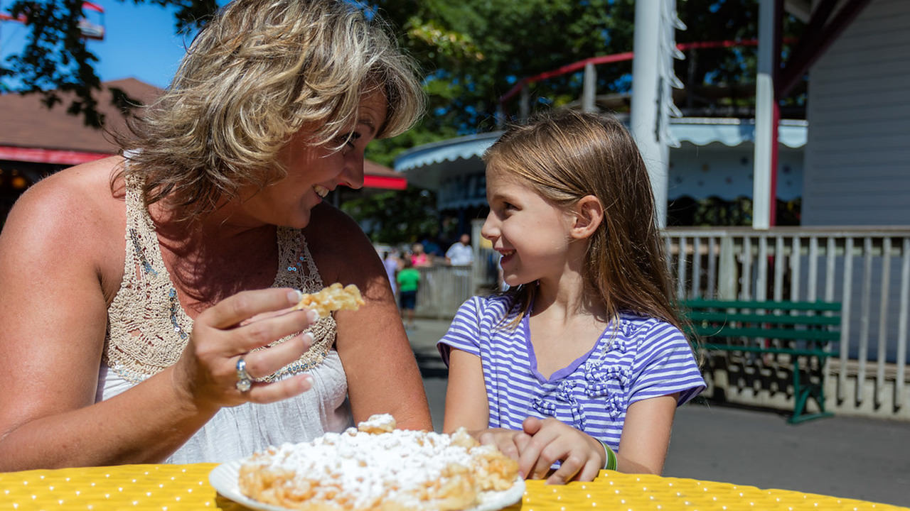 An adult and a child enjoying a funnel cake.